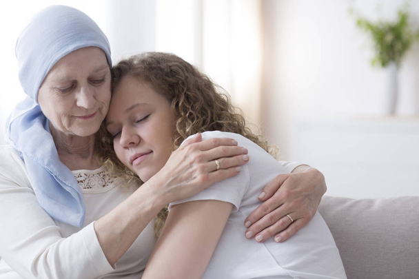 Daughter hugging sick elderly mother with cancer wearing a blue headscarf - Foto, Bild