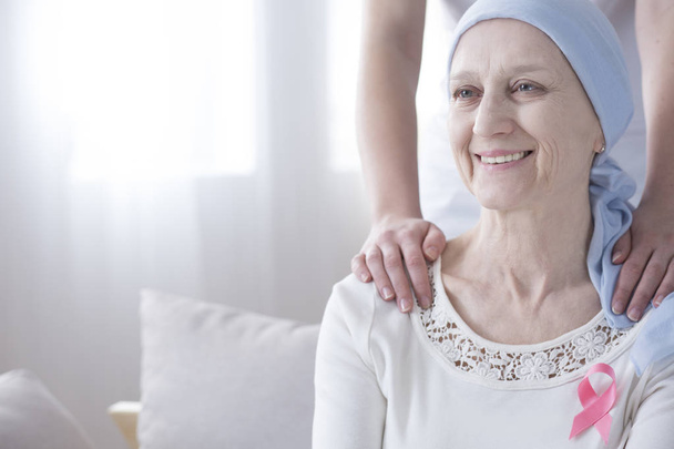Szczęśliwy starszą kobietę z rakiem piersi na sobie różową wstążką, obsługiwane przez opiekuna - Zdjęcie, obraz