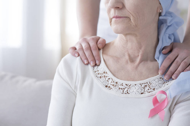 Sick woman wearing a pink breast cancer ribbon supported by her daughter - Foto, immagini