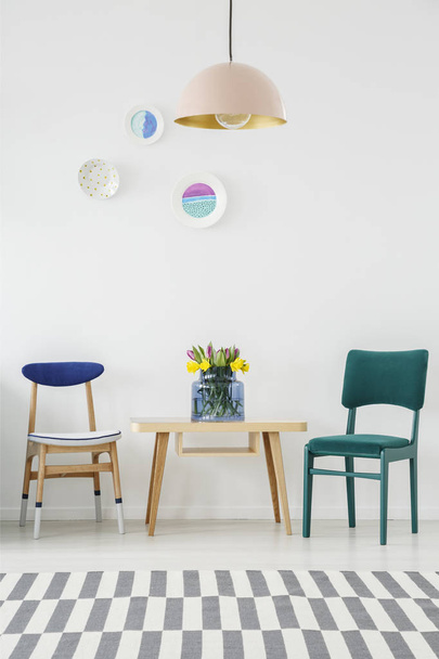 Turquoise chair next to a wooden table with flowers under pastel lamp in dining room interior - Foto, afbeelding