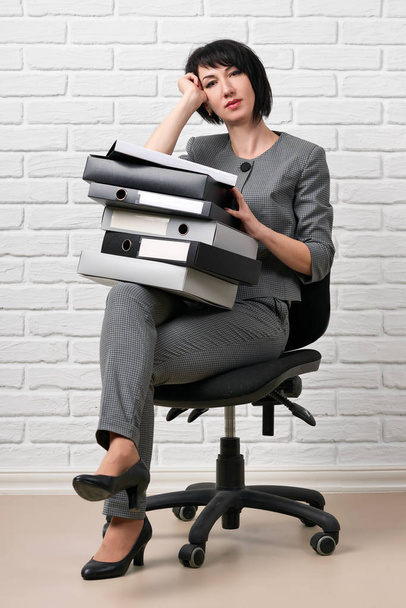 mulher de negócios com pasta, vestida com um terno cinza posa na frente de uma parede branca
 - Foto, Imagem
