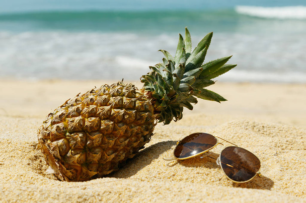 Pineapple and sunglasses on sandy beach, close up view - Fotoğraf, Görsel