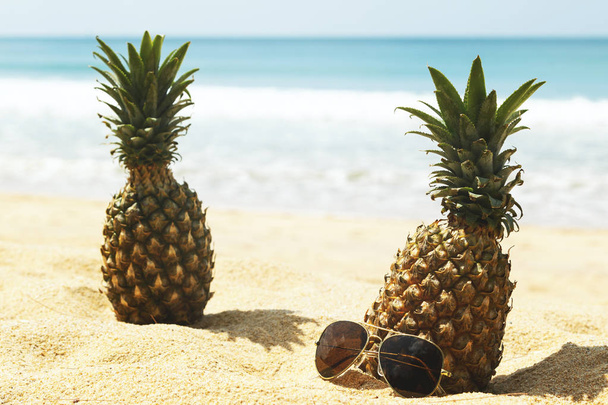 Pineapples and sunglasses on sandy beach, close up  - Фото, изображение