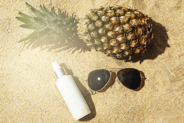 Pineapple, sunglasses and sunscreen lotion on the beach - Photo, Image