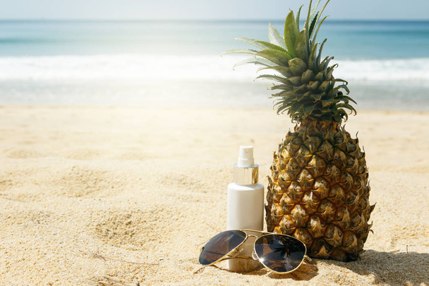 Pineapple, sunglasses and sunscreen lotion on the beach - Photo, image
