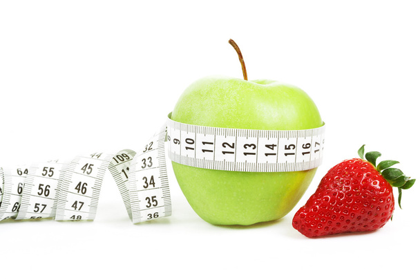 Measuring tape wrapped around a green apple and strawberry as a symbol of diet - Foto, Imagen