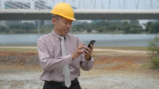 Asiático senior hombre de negocios en traje y casco amarillo usando el teléfono
 - Imágenes, Vídeo