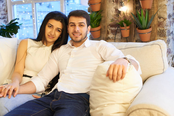 glücklicher Ehemann mit Frau sitzt zusammen auf weißem Sofa in Wohnung  - Foto, Bild