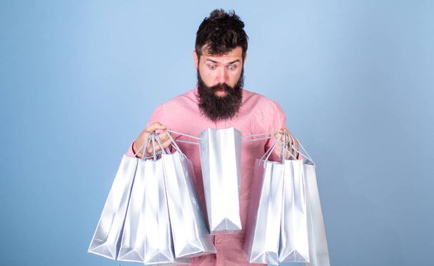 Sale and discount concept. Hipster on shocked face shopping addicted or shopaholic. Man with beard and mustache carry shopping bags, light blue background. Guy shopping on sales season with discounts - Fotó, kép