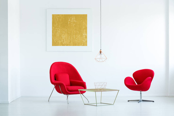 Red armchairs at gold table in minimal white flat interior with yellow painting and lamp. Real photo - Photo, Image