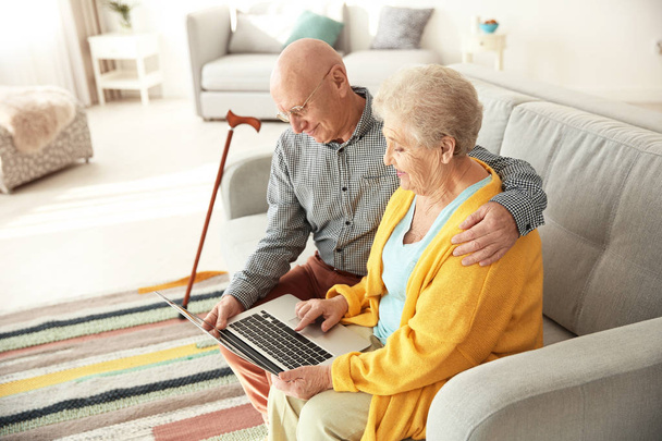 Elderly couple using laptop in living room - Fotoğraf, Görsel