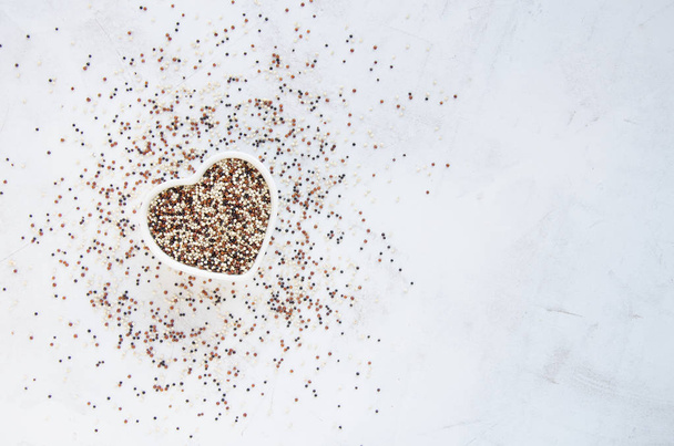 Red, white and black quinoa seed mix in a heart shaped bowl on rustic surface, top view - Foto, afbeelding