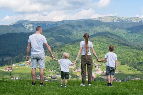Οικογενειακές διακοπές. Γονείς και οι δύο γιοι θαυμάστε την θέα της κοιλάδας. Βουνά στο βάθος. Πίσω όψη - Φωτογραφία, εικόνα