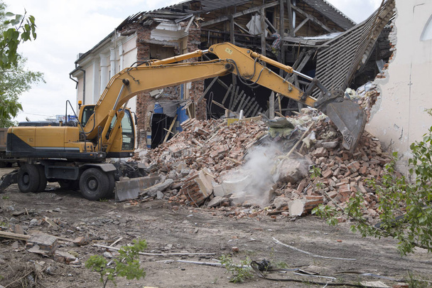 La destrucción de las paredes del antiguo edificio y la limpieza de los escombros de la construcción con un cubo de una excavadora. - Foto, imagen