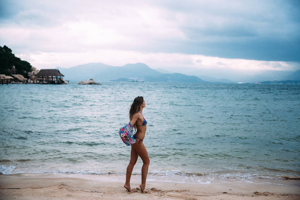 Vista lateral de uma menina esbelta sexy posando contra uma água azul azure na areia branca. Conceito de descanso, praia, viagem
. - Foto, Imagem