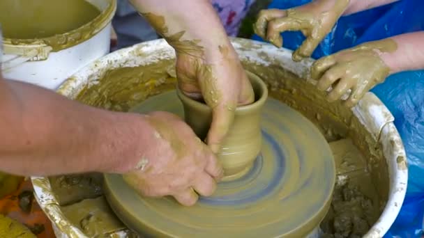 Руки горшечника имеют форму чаши из глины. Процесс создания керамики на гончарном круге. Мастер керамики учит ученика делать кастрюлю в своей студии. Крупный план, только руки
. - Кадры, видео