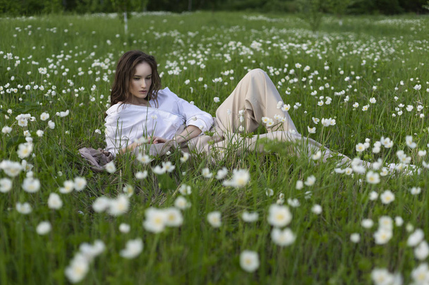 Piękna stylowa dziewczyna sobie modną koszulę, beżowe majtki i pareo relaksujący znajduje się na zielonej trawie, pośród dzikich kwiatów. Handlowych i ogłoszenie projektu. Miejsce. - Zdjęcie, obraz