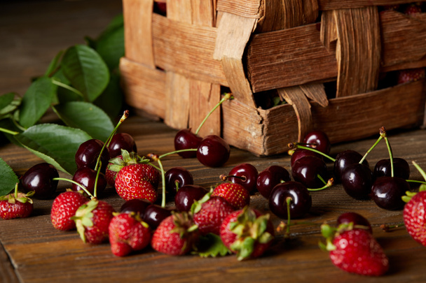 reife Kirschen und Erdbeeren auf Holzoberfläche mit Blättern und rustikaler Schachtel - Foto, Bild