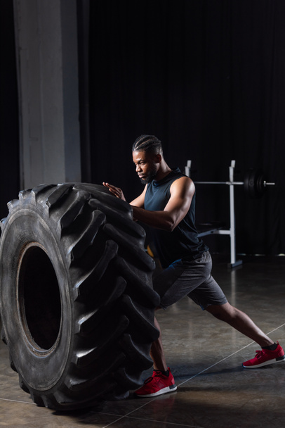 side view of muscular young african american sportsman exercising with tire   - 写真・画像