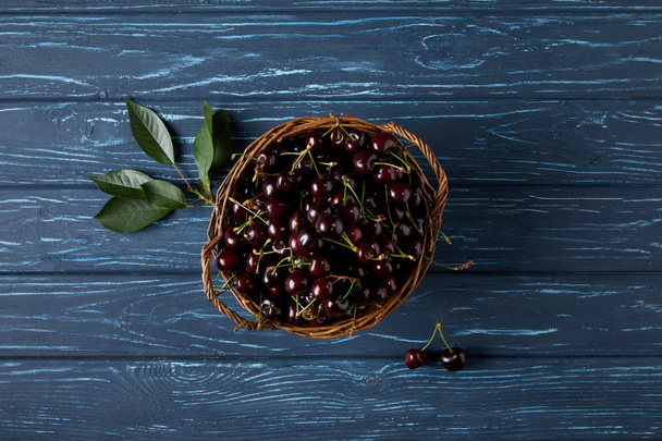 top view of ripe sweet cherries in rustic basket on blue wooden surface - 写真・画像