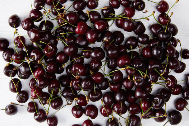 top view of fresh ripe sweet cherries spilled on white wooden surface - Photo, Image