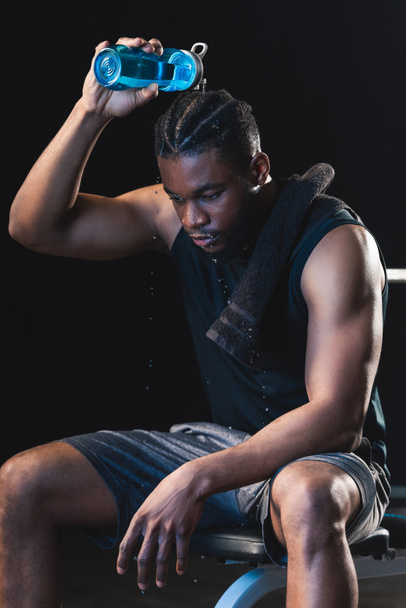 tired african american sportsman pouring water on head while sitting after workout in gym - Zdjęcie, obraz