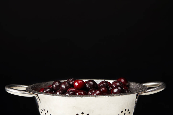 fresh ripe cherries in colander isolated on black - 写真・画像