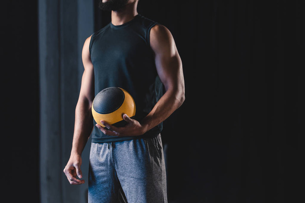 обрізаний знімок м'язистого афроамериканця в спортивному одязі, що тримає м'яч
 - Фото, зображення