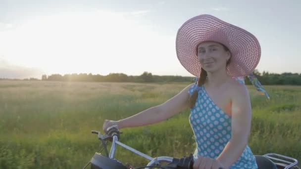 Una joven feliz en un sombrero monta una motocicleta retro y disfruta de un paseo en un camino de tierra entre los campos y prados
 - Imágenes, Vídeo