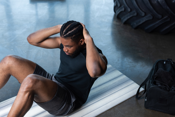vista de ángulo alto del hombre afroamericano muscular haciendo abdominales en el gimnasio
 - Foto, imagen