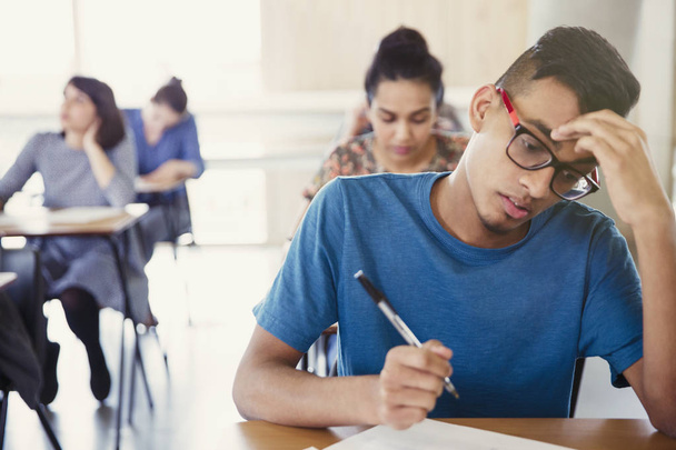 Серьезный студент колледжа сдает экзамен за партой в классе
 - Фото, изображение