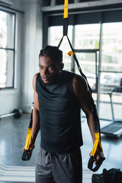 serious young african american sportsman training with fitness straps in gym - Photo, Image