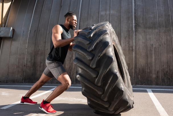 muskulöser afrikanisch-amerikanischer Sportler trainiert mit Reifen auf der Straße   - Foto, Bild
