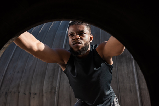 view through tyre of young african american man exercising on street - Photo, Image