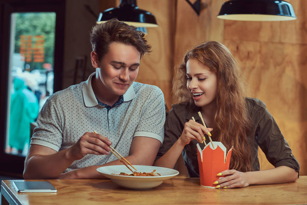 Heureux jeune couple portant des vêtements décontractés manger des nouilles épicées dans un restaurant asiatique
. - Photo, image