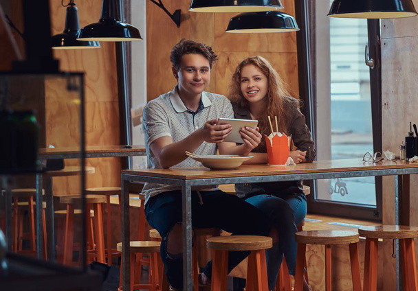 Feliz casal de jovens estudantes usando um tablet digital durante a pausa para o almoço em um restaurante asiático
.  - Foto, Imagem