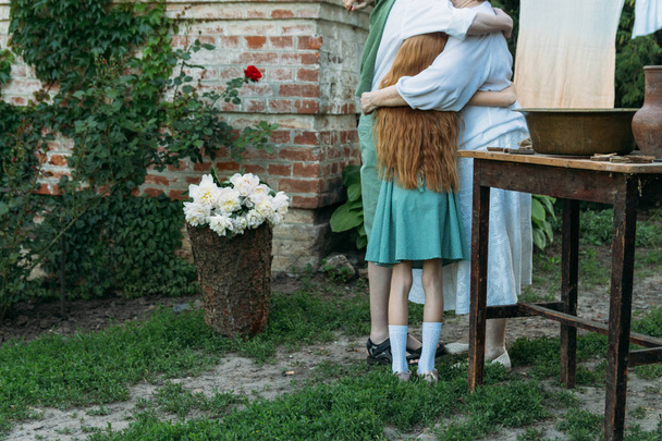 meeting grandmother and grandchildren. grandmother embraces grandchildren, brother and sister. grandson and granddaughter came to visit. give flowers. relatives meeting. Grandmother in white vintage clothing and grandchildren in green clothes. next t - Foto, Bild