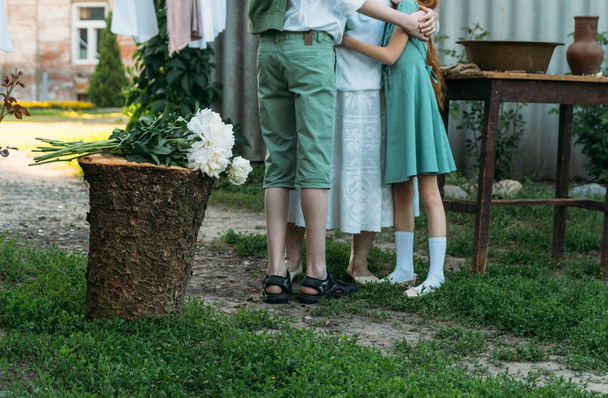 meeting grandmother and grandchildren. grandmother embraces grandchildren, brother and sister. grandson and granddaughter came to visit. give flowers. relatives meeting. Grandmother in white vintage clothing and grandchildren in green clothes. next t - Photo, image