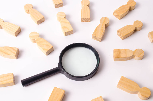 Wooden figures of people lie around a magnifying glass on a white background. Hiring for work, tracing people. The concept of the search for people and workers, human resources. - Foto, afbeelding