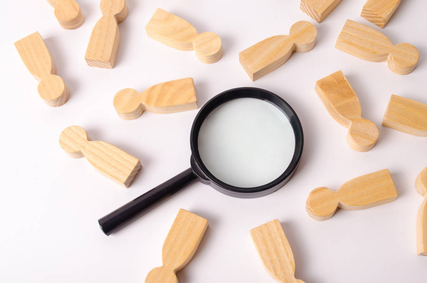 Wooden figures of people lie around a magnifying glass on a white background. Hiring for work, tracing people. The concept of the search for people and workers, human resources. - 写真・画像