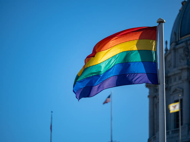 A gay pride flag waving in air with United States flag in background - Photo, Image