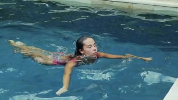 Una deportista sexy navega en la piscina, disfruta de un cálido día de verano, emerge del agua, se convierte en codos en el lado de la piscina. Una toma lenta de una hermosa chica flotante de apariencia europea
. - Metraje, vídeo