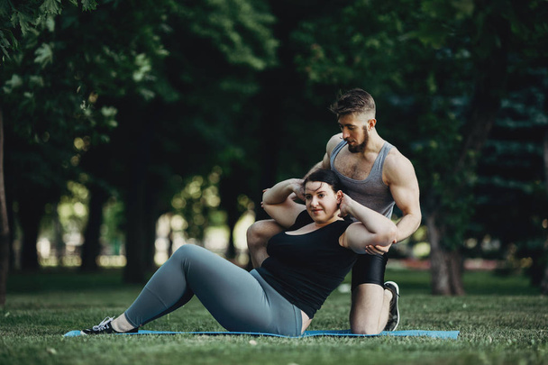 Obese woman doing sit-ups with personal trainer - Foto, immagini