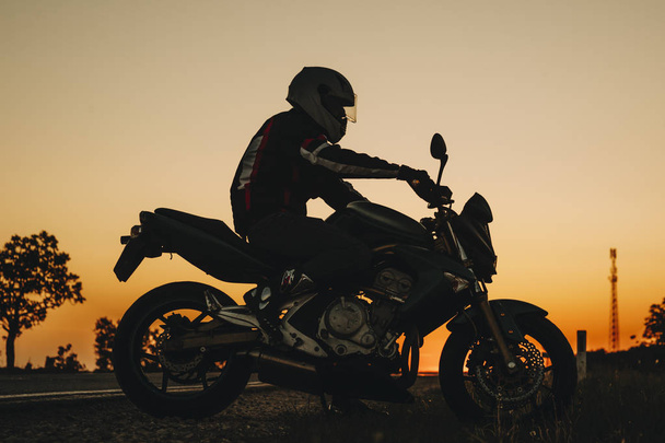 Side view of man in helmet riding on dark road on motorbike at sunset in countryside - Foto, Bild