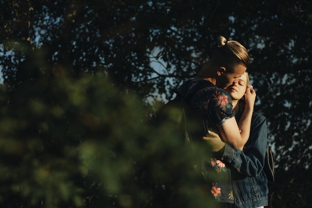 Gewas weergave van aantrekkelijke man teder verbonden zijn sierlijke roze bloem aan haar achter oor van mooie jonge blonde vrouw knuffelen hem met gesloten ogen - Foto, afbeelding