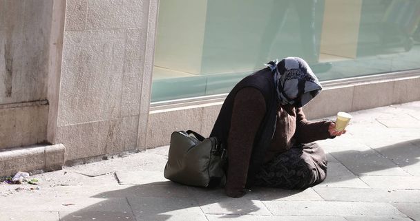 Цыганка просит милостыню, сидя на земле со стеклом
 - Фото, изображение