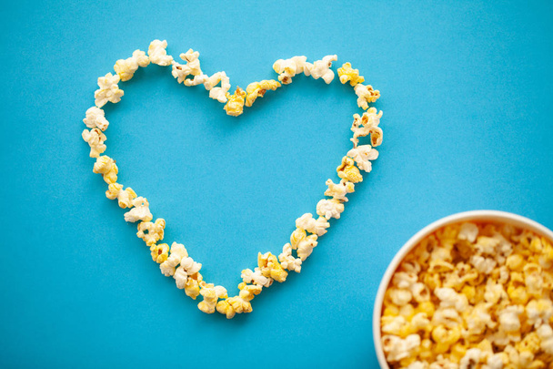 Voedsel. Afbeelding van het hart vormen van Popcorn. Emmer popcorn. Heerlijke Popcorn op blauwe achtergrond. Bioscoop. - Foto, afbeelding
