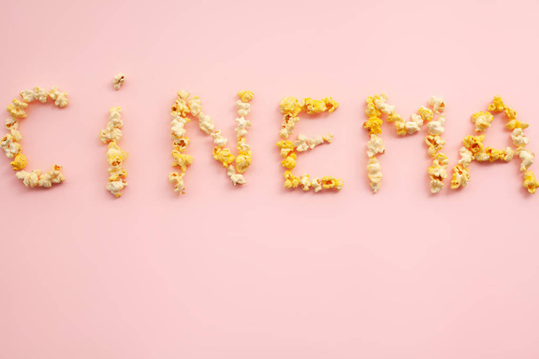 Еда. Слово веселья. Ведро с попкорном. Вкусный попкорн на розовом фоне. Кино
. - Фото, изображение