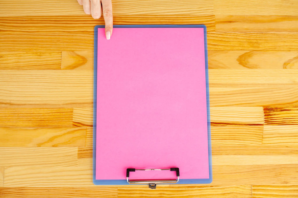 Main de bureau tenant un dossier avec un papier de couleur rose sur le fond de la table en bois. Copyspace. Place pour le texte
. - Photo, image