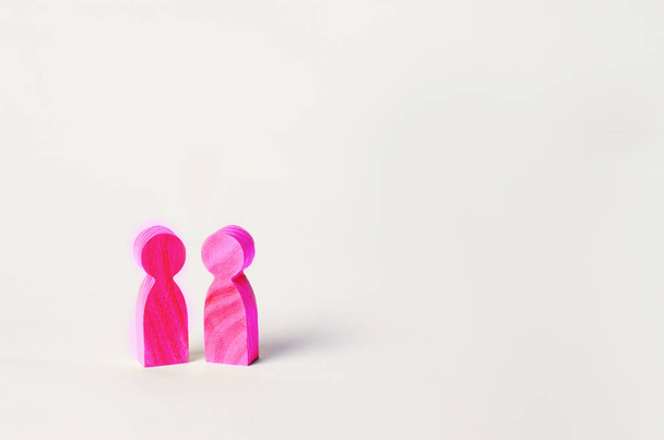 two pink wooden figures of people stand on white background. two persons of homosexual orientation. the concept of the relationship between lesbians and representatives of gender minorities. Lifestyle. copy space - Fotó, kép